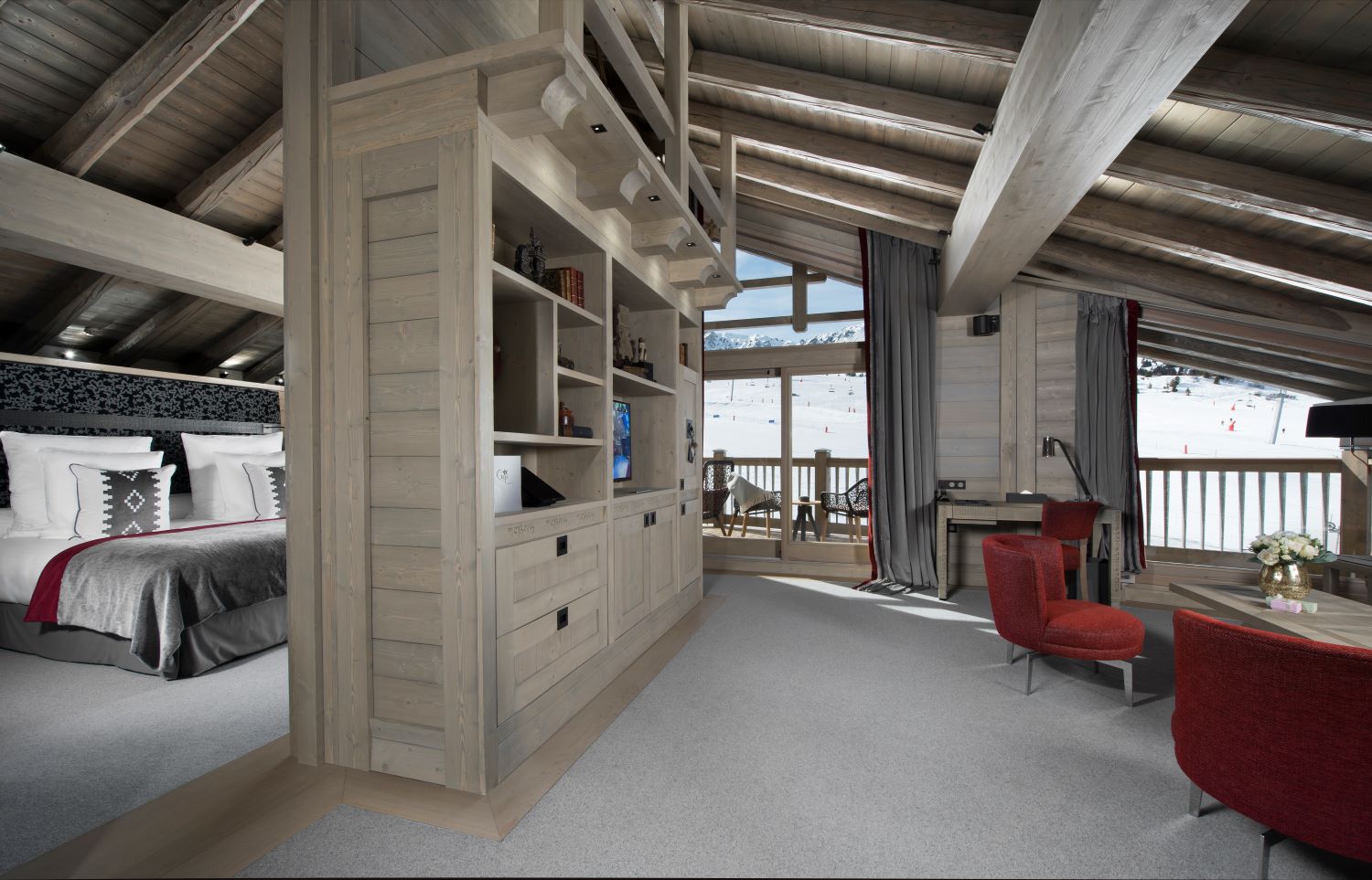 Hotel Le K2 Altitude Courchevel - Loft style suite with large bedroom area dividing storage unit with tv and drawers and seating area with chair coffee table and writing desk plus access to private balcony