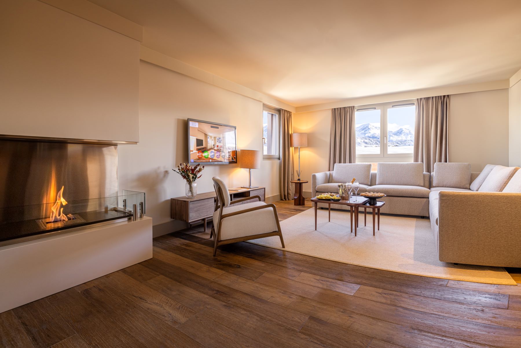 Les Suites de la Potinière Courchevel - Large bright sitting room with L shaped sofa chair fireplace and duel aspect windows with mountain views